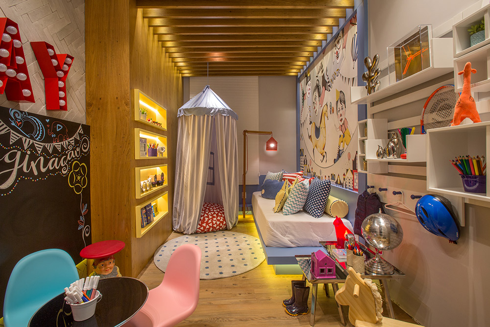 CASACOR Rio de Janeiro 2016. Quarto da Imaginação - Paula Costa. O quarto de brincar dispensa TV ou tablet. Ele tem muitos livros e espaço de leitura na cabana produzida pela By Floor. Até peças consagradas de design vêm com cara de criança, como as cadeiras Panton. No papel de parede Join the Circus, da designer Adelina Mehmeti, é possível substituir o rosto dos personagens por fotos da família e dos amigos.