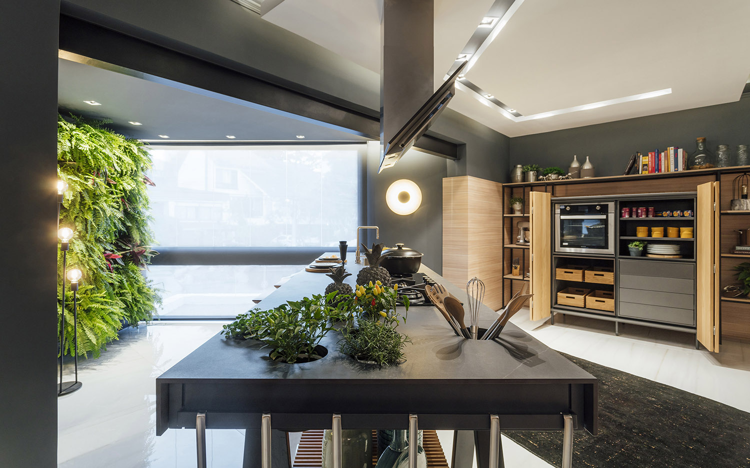 Atelier Culinário - W4 Arquitetura. A arte de cozinhar ganha um atelier à altura, que se desenvolve em torno da grande bancada. Ela é produzida em Dekton Kelya, com espaço para horta integrada e base ripada em lâminas de Carvalho natural. A marcenaria tem ares de armazém, com design de La Agencia, inspirada nas cozinhas de décadas passadas. A vegetação é farta, para trazer vida e frescor.