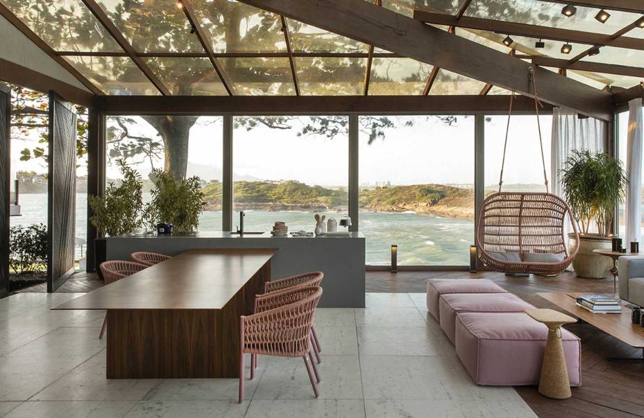 Lounge Sunset - Cyane Zoboli. A arquitetura se integra à paisagem e amplia o alcance da visão, sem perder o conforto de estar em casa. O ambiente de 130 m² emoldura a vista da baía de Vitória e aposta nos recursos naturais, como a madeira e o vidro que conferem simplicidade à estrutura. A ambientação projetada não veio ao acaso, destacando o uso de materiais rochosos, como granito e ardósia, e de madeiras para o deck e mobiliário.