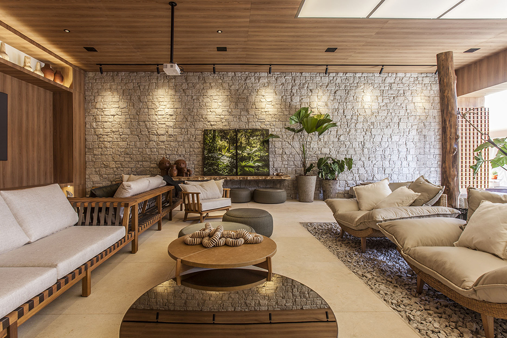 CASACOR Brasília 2019. Nosso Recanto - Larissa Dias. Com 128 m², o ambiente foi pensado para ser uma forma relaxante de se reconectar com a natureza. Em meio à redes, pufes e almofadas em ráfia e fibras naturais, uma parede de pedras captura o olhar acrescenta texturas e linhas ao espaço.