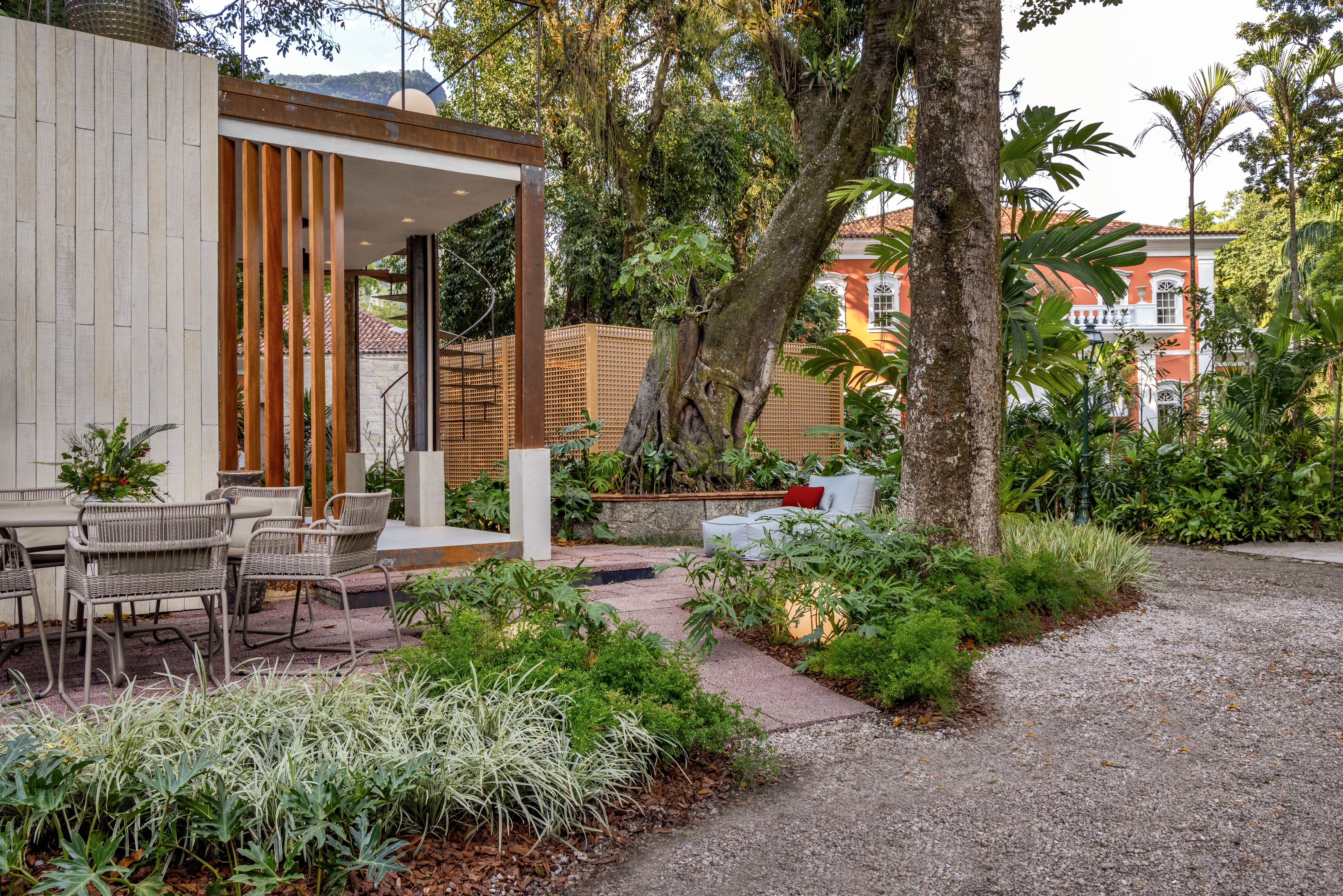 Karyne Lima - Jardim Caminhos e Conexões. Para o bangalô Caminhos, a paisagista Karyne Lima criou um jardim com vegetação bem tropical, como toda a mata que já ocupa a área externa do Instituto Brando Barbosa. Mas aqui o que chama a atenção é a diversidade de texturas e tonalidades das folhagens verdes. São espécies como Dionela, Bipinnatifidum, Liriope e Ravenala que criam um caminho orgânico, como se sempre estivessem estado ali. E elas aparecem também no telhado do bangalô, que reproduz este traçado em linhas curvas criando um gostoso ambiente extra de estar, de onde se pode apreciar todo o jardim.